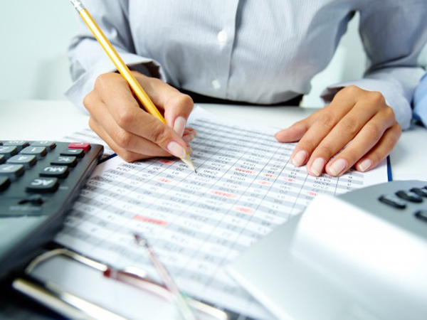 Trabajador escribiendo sobre hoja de papel junto a calculadoras