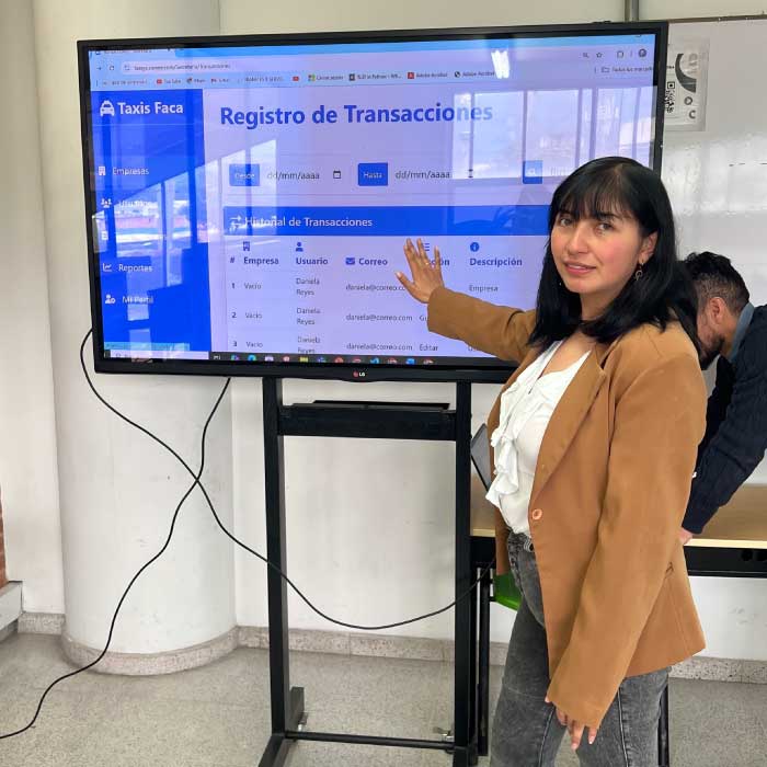 Fotografía de estudiante señalando una pantalla con una aplicación llamada Taxis Fácil
